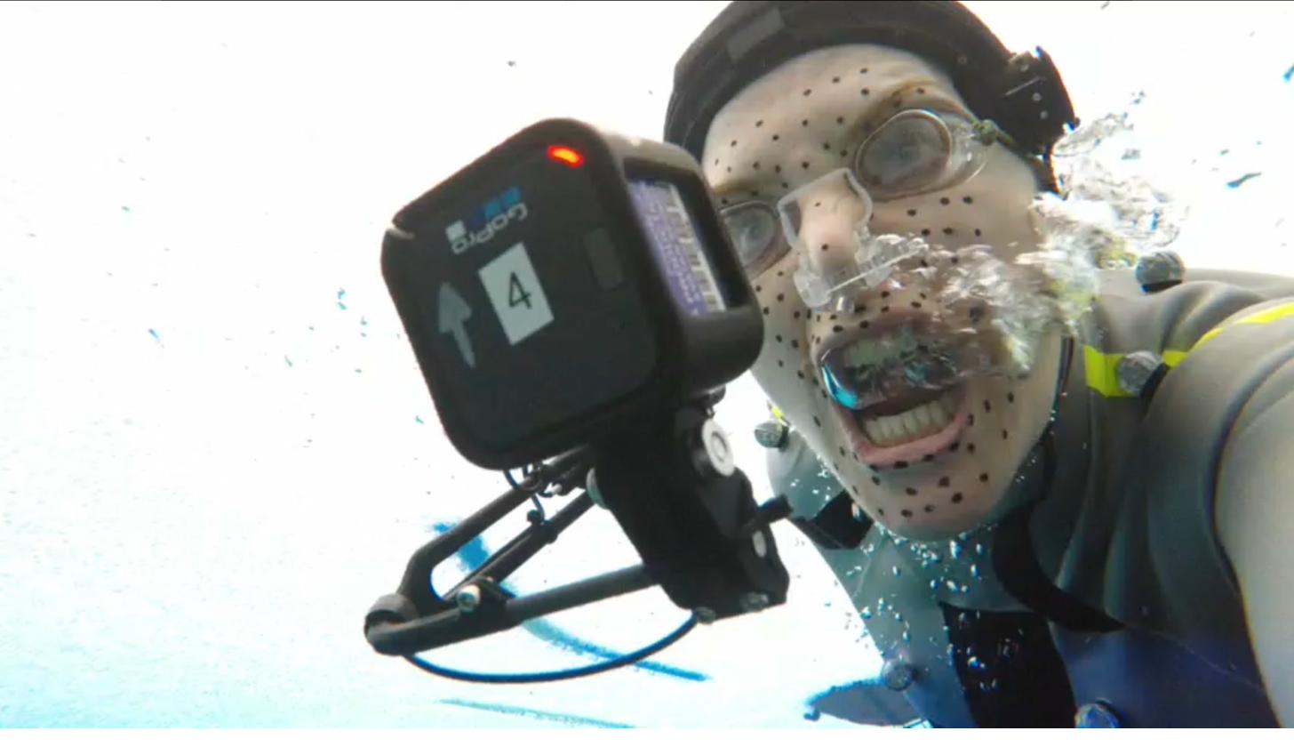 An actor performing underwater in full mocap suit with GoPro camera rig in the performance capture tank