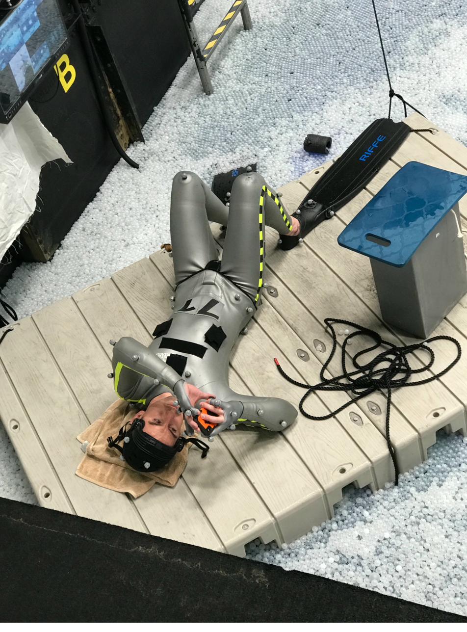 A stunt performer resting on a platform at the edge of the ball pit tank in full mocap suit