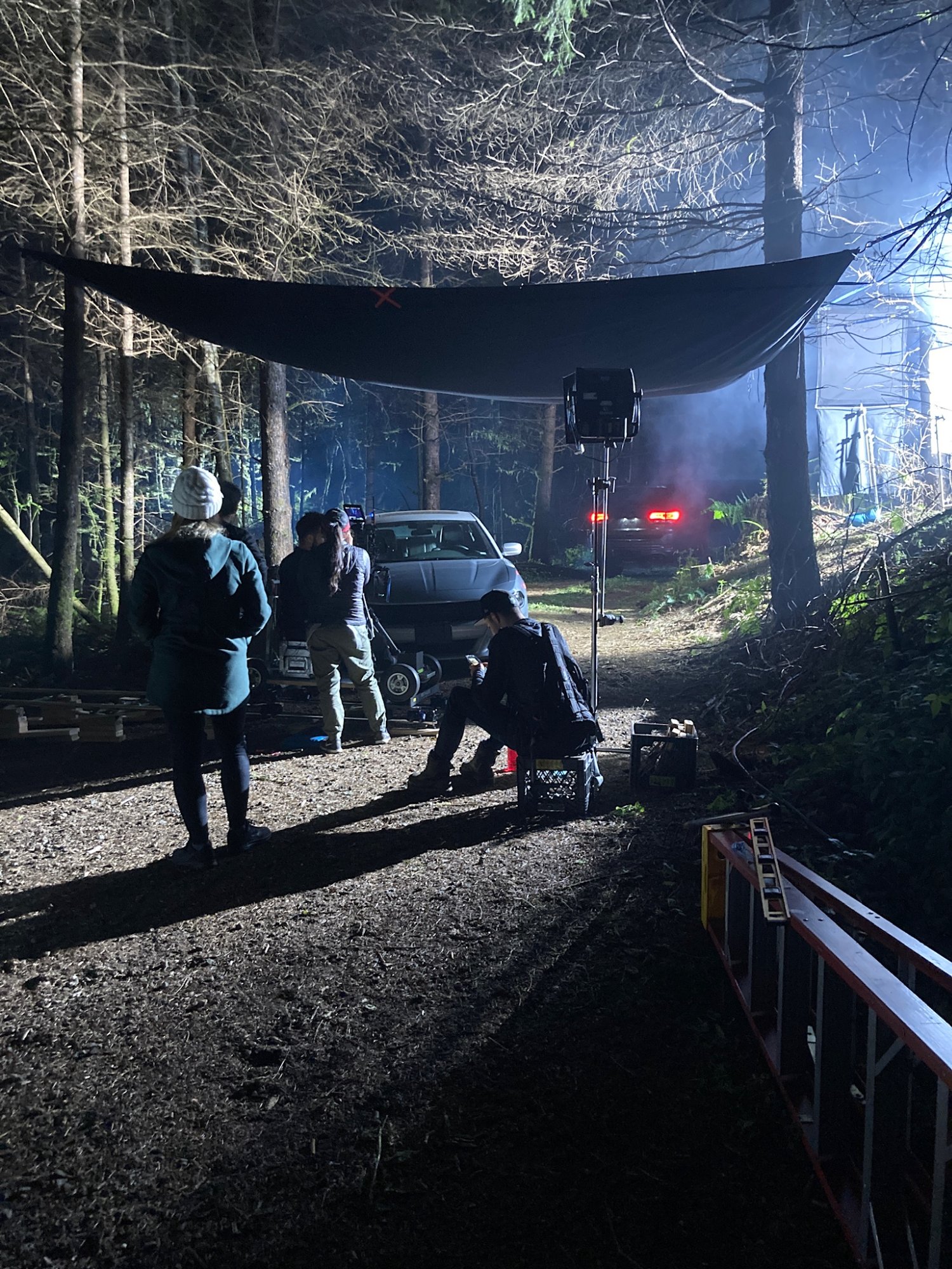 Night exterior base camp under a tarp in the Oregon forest — crew between takes