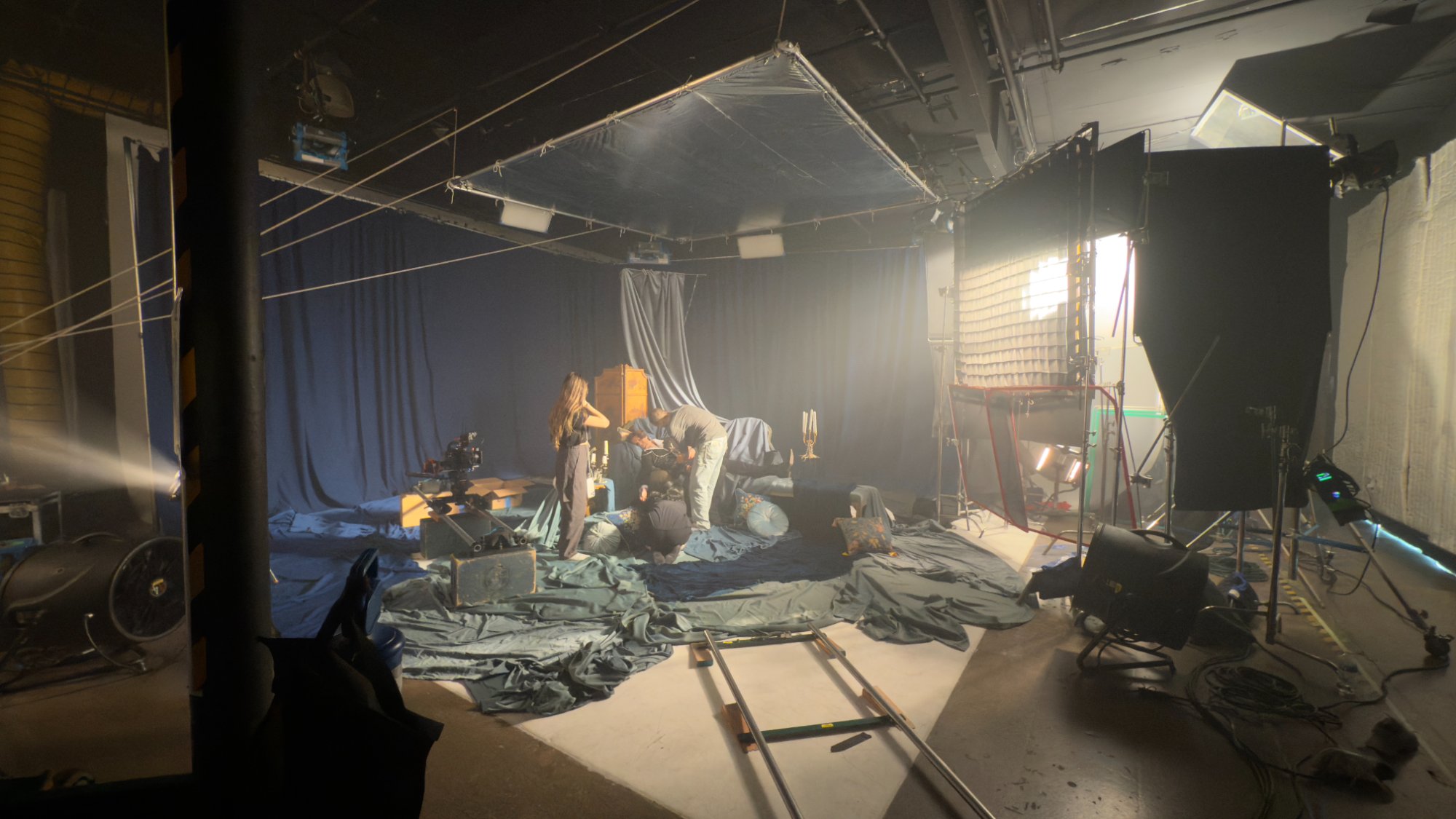 Wide BTS of the Rococo set — blue drapes, candelabras, layered soft light from a large key with bounce, dolly track in foreground