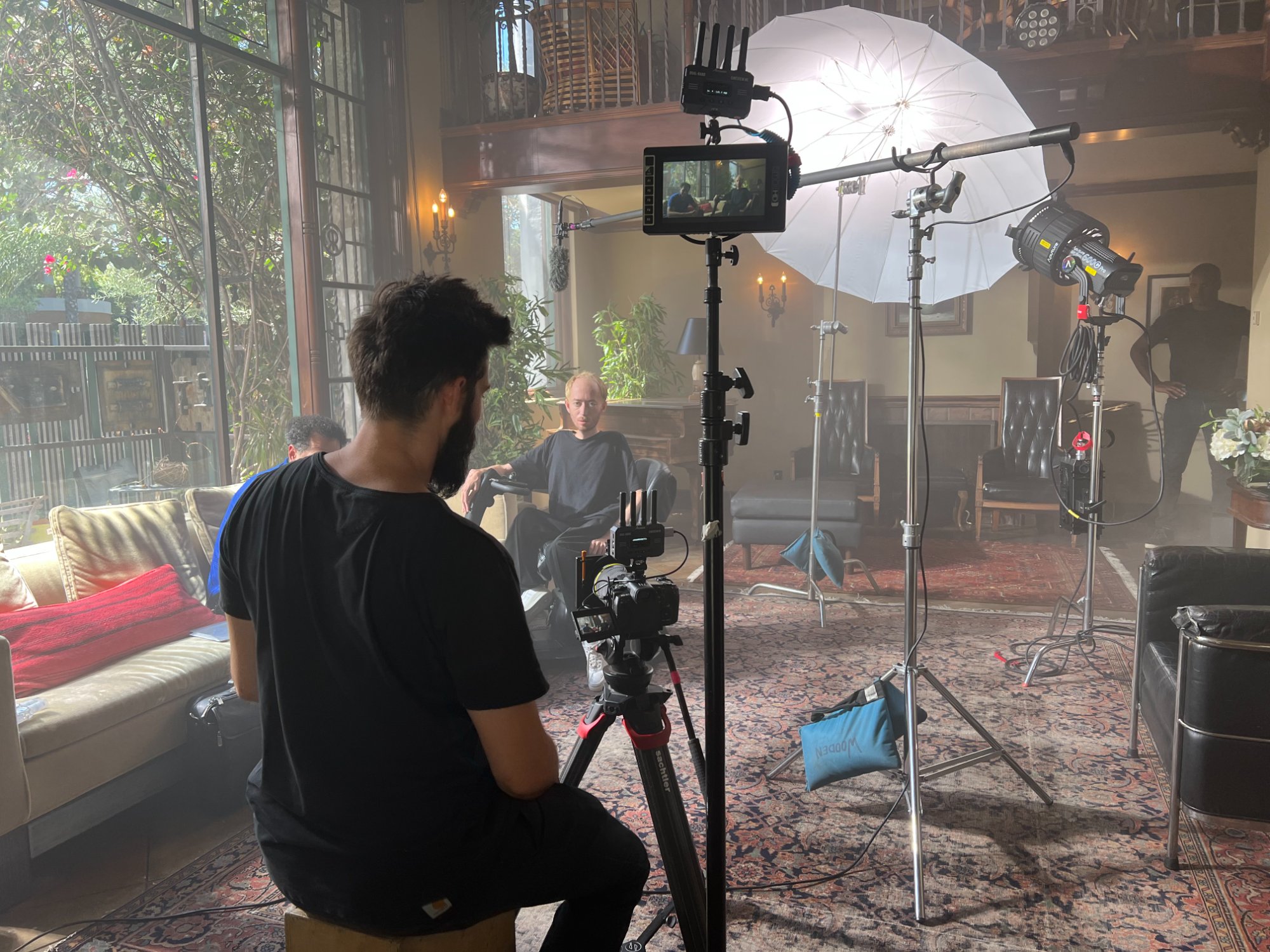 Nathan shooting Danny's interview — umbrella key, natural window light mixing with practicals in a living room location